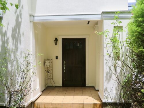 白い壁に、深い茶色の木製ドアが印象的な玄関です(玄関)
